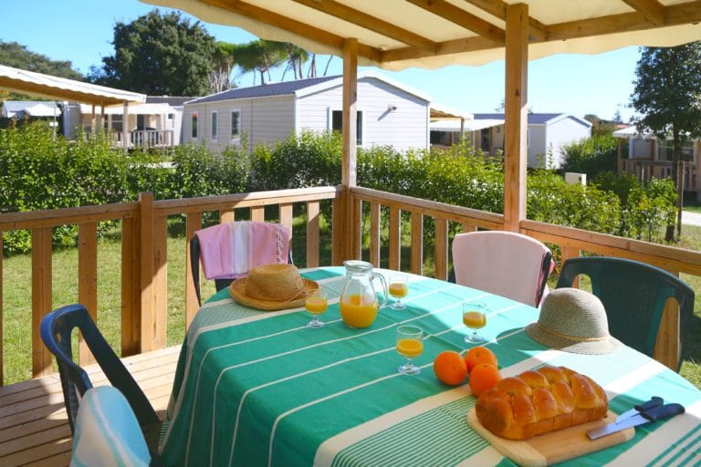 Terrasse ensoleillée avec petit déjeuner, mobil-homes en arrière-plan.